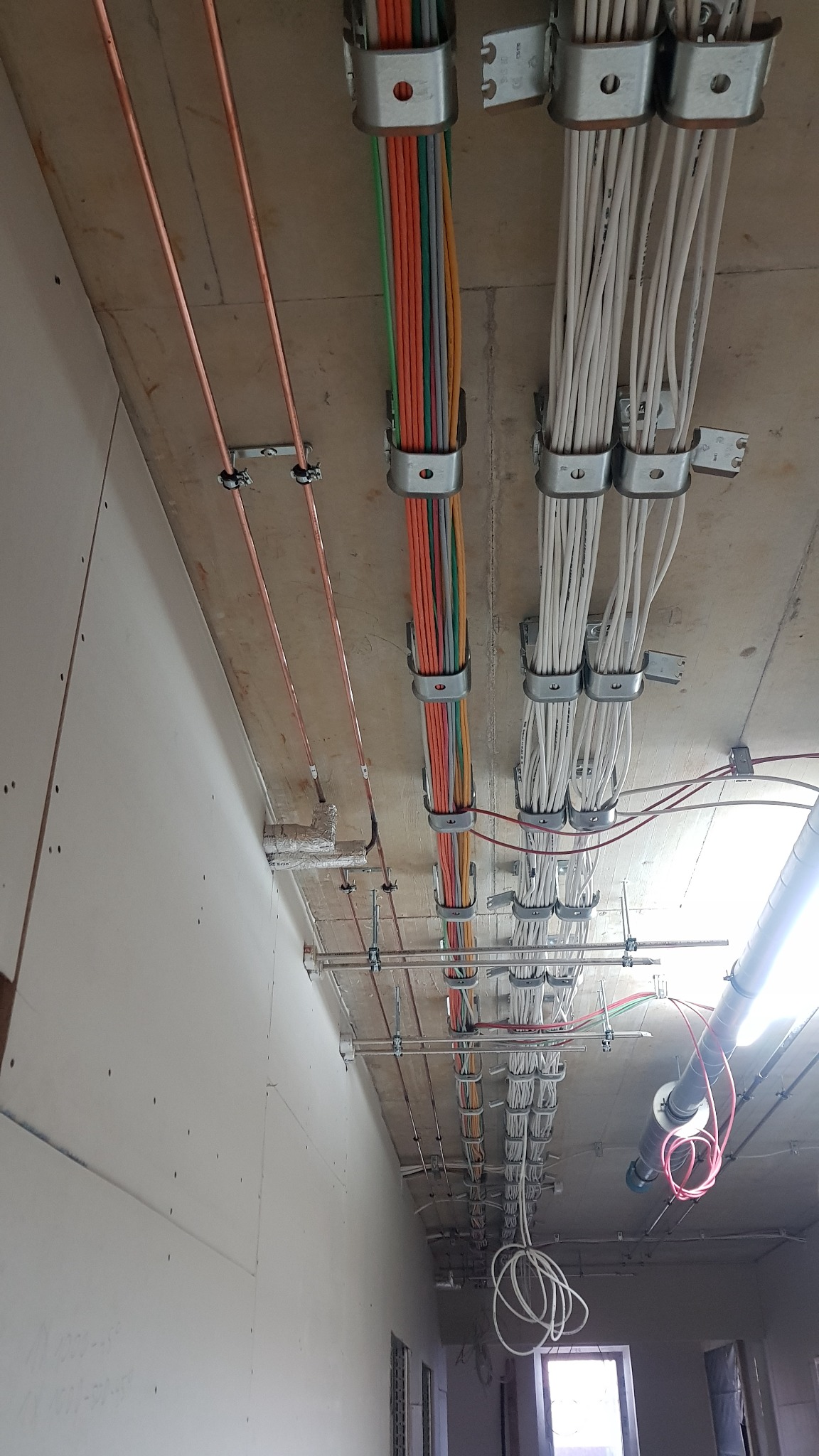 Kable elektryczne różnego koloru, prowadzone pod sufitem, zamocowane metalowymi uchwytami, widoczne elementy instalacji wentylacyjnej.