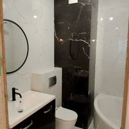 Prywatnie - Nowoczesna łazienka z czarno-białymi marmurkowymi płytkami, okrągłym lustrem, czarną armaturą, podwieszaną toaletą i geometrycznymi lampami sufitowymi.