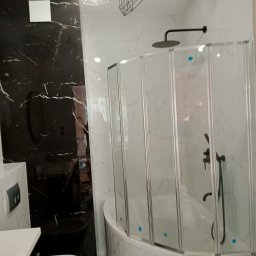 Prywatnie - Nowoczesna łazienka z czarno-białymi marmurowymi płytkami, kabiną nawannową ze składanymi drzwiami i geometrycznymi lampami sufitowymi.