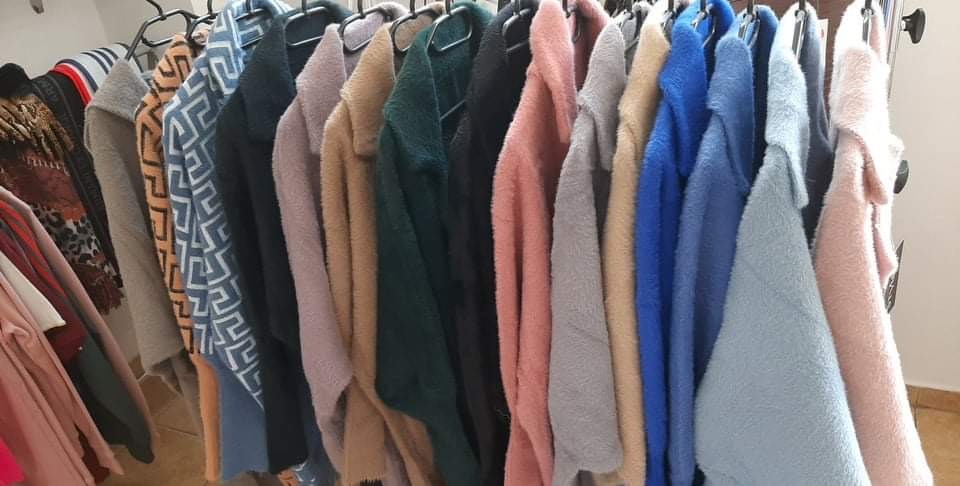 Różnokolorowe, puszyste swetry i kardigany wiszące na wieszakach, widoczne różne wzory i faktury materiałów.