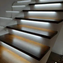 Nowoczesne, drewniane schody z podświetleniem LED na każdym stopniu, widok z dołu, marmurowa ściana w tle.