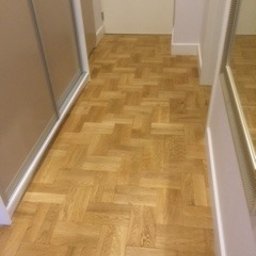 Ryszard Godo - Parkiet ułożony w jodełkę w jasnym korytarzu, widoczne drzwi i fragment szafy wnękowej.