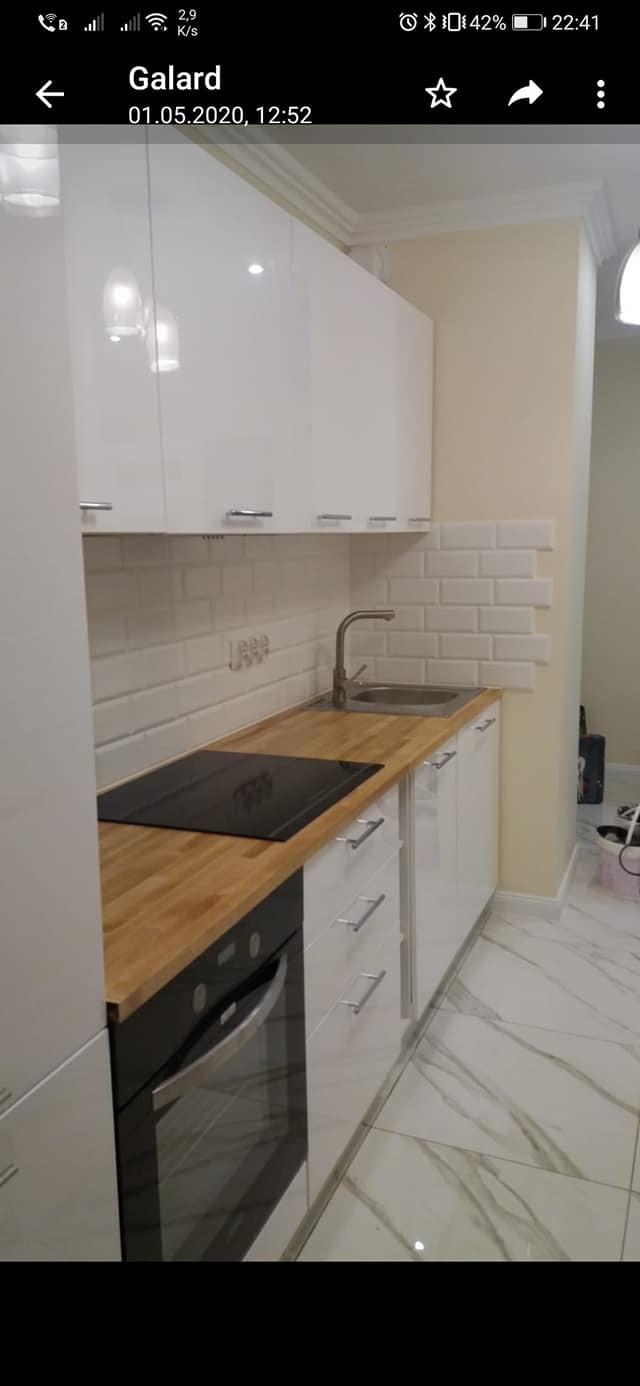 Nowoczesna kuchnia z białymi, błyszczącymi szafkami, drewnianym blatem i białymi kafelkami w stylu metro, z widoczną płytą grzewczą i piekarnikiem.