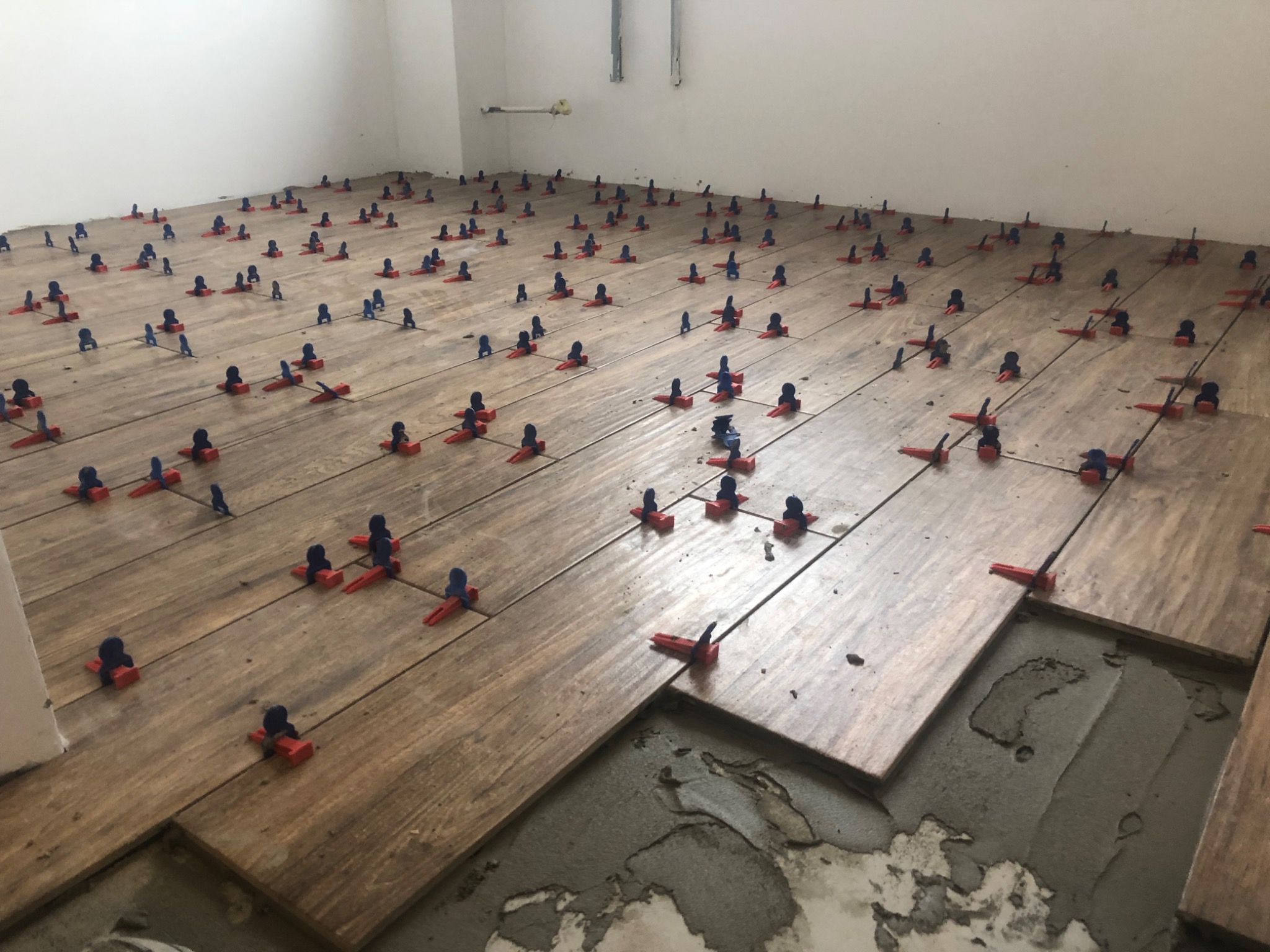 Ułożone płytki imitujące drewno z systemem poziomowania płytek (klipsy i kliny) na podłodze w trakcie prac wykończeniowych, widoczne zaprawy i niedokończony fragment podłogi.