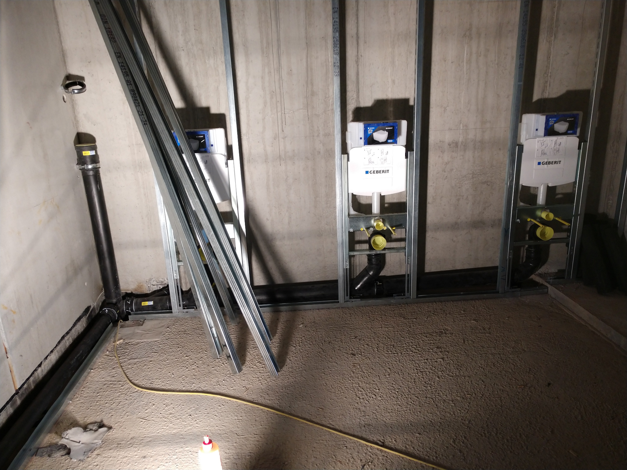 Montaż stelaży podtynkowych Geberit w łazience w trakcie remontu, widoczne rury kanalizacyjne i profile metalowe.