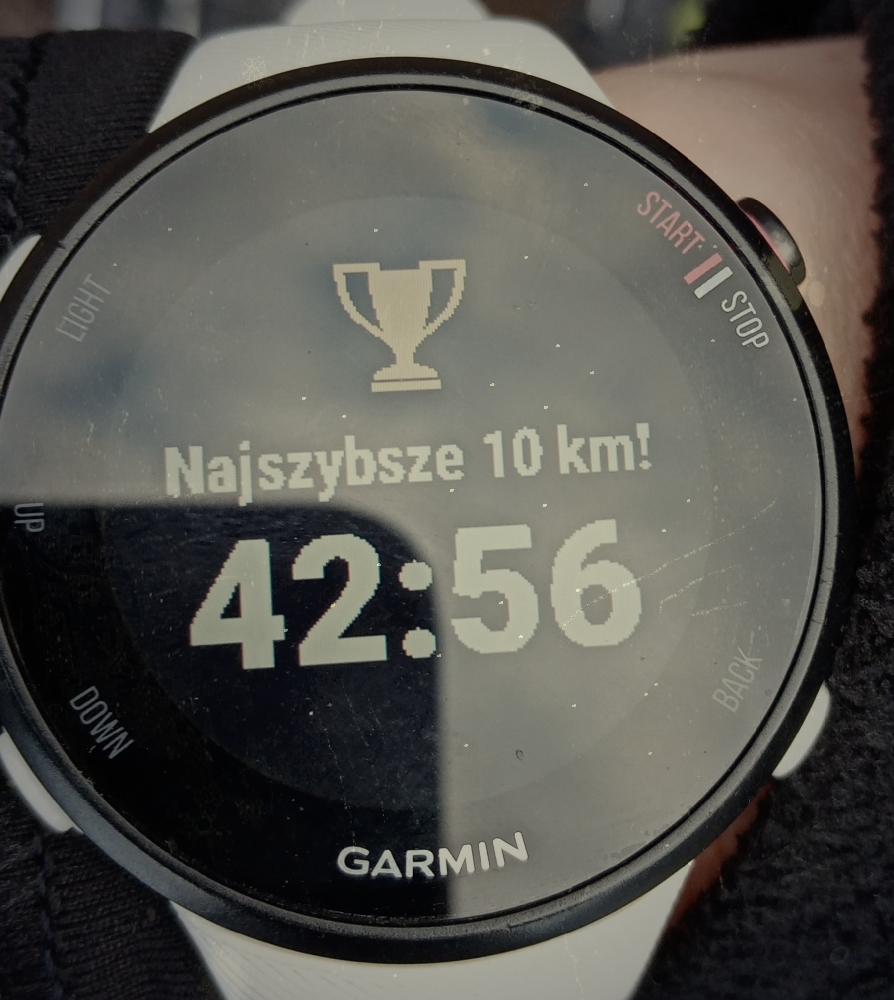 Zegarek sportowy Garmin wyświetlający czas 42:56 i informację o najszybszym biegu na 10 km oraz ikonę pucharu.