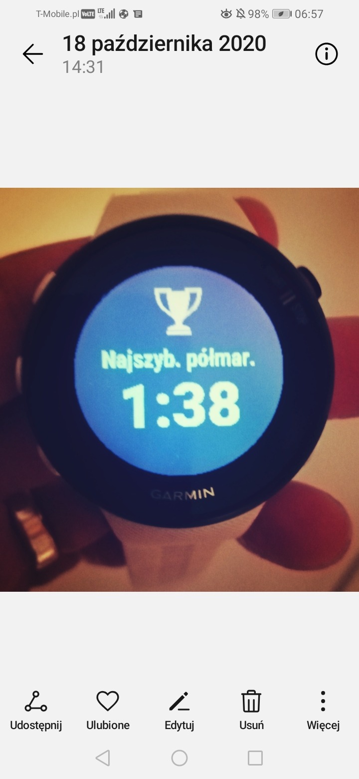 Zegarek Garmin z wyświetlonym rekordem: 1:38 w półmaratonie, widoczny puchar symbolizujący sukces.