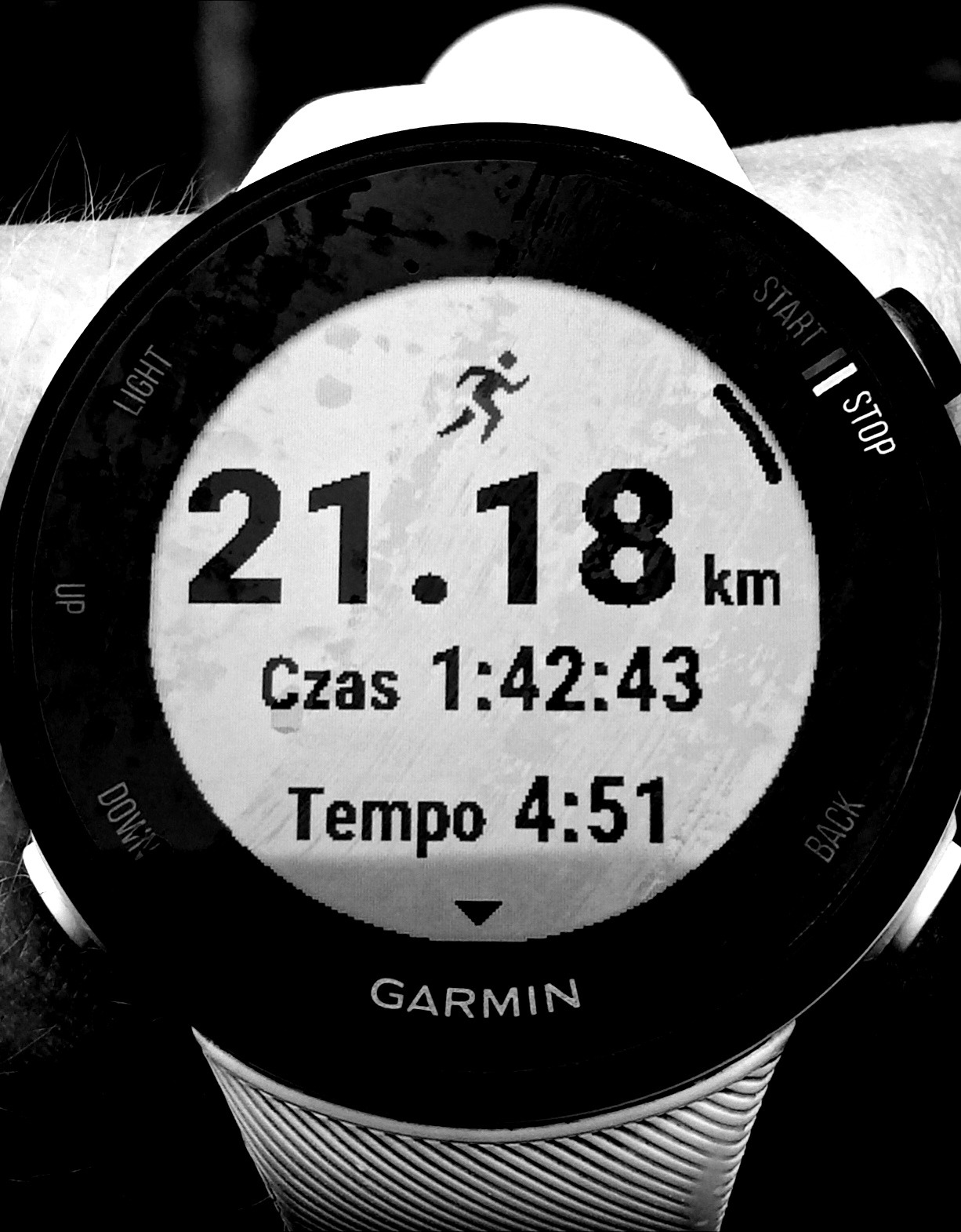 Czarno-białe zdjęcie zegarka sportowego Garmin na nadgarstku, wyświetlającego dystans 21.18 km, czas 1:42:43 i tempo 4:51, wskazujące na ukończony bieg.
