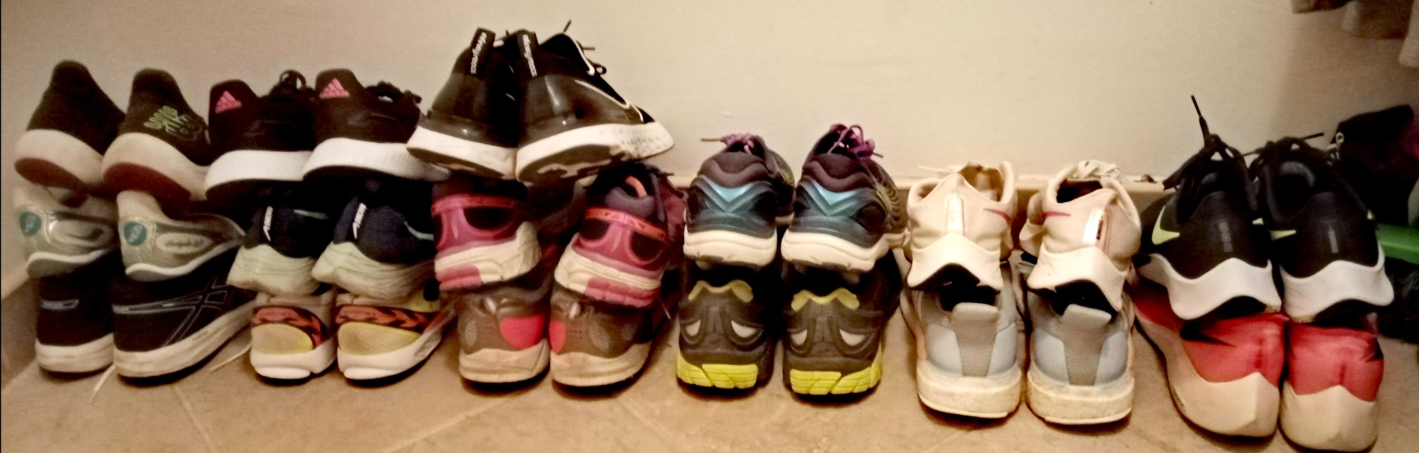 Rząd używanych butów sportowych różnych marek, ustawionych piętami do widza na podłodze wzdłuż ściany.