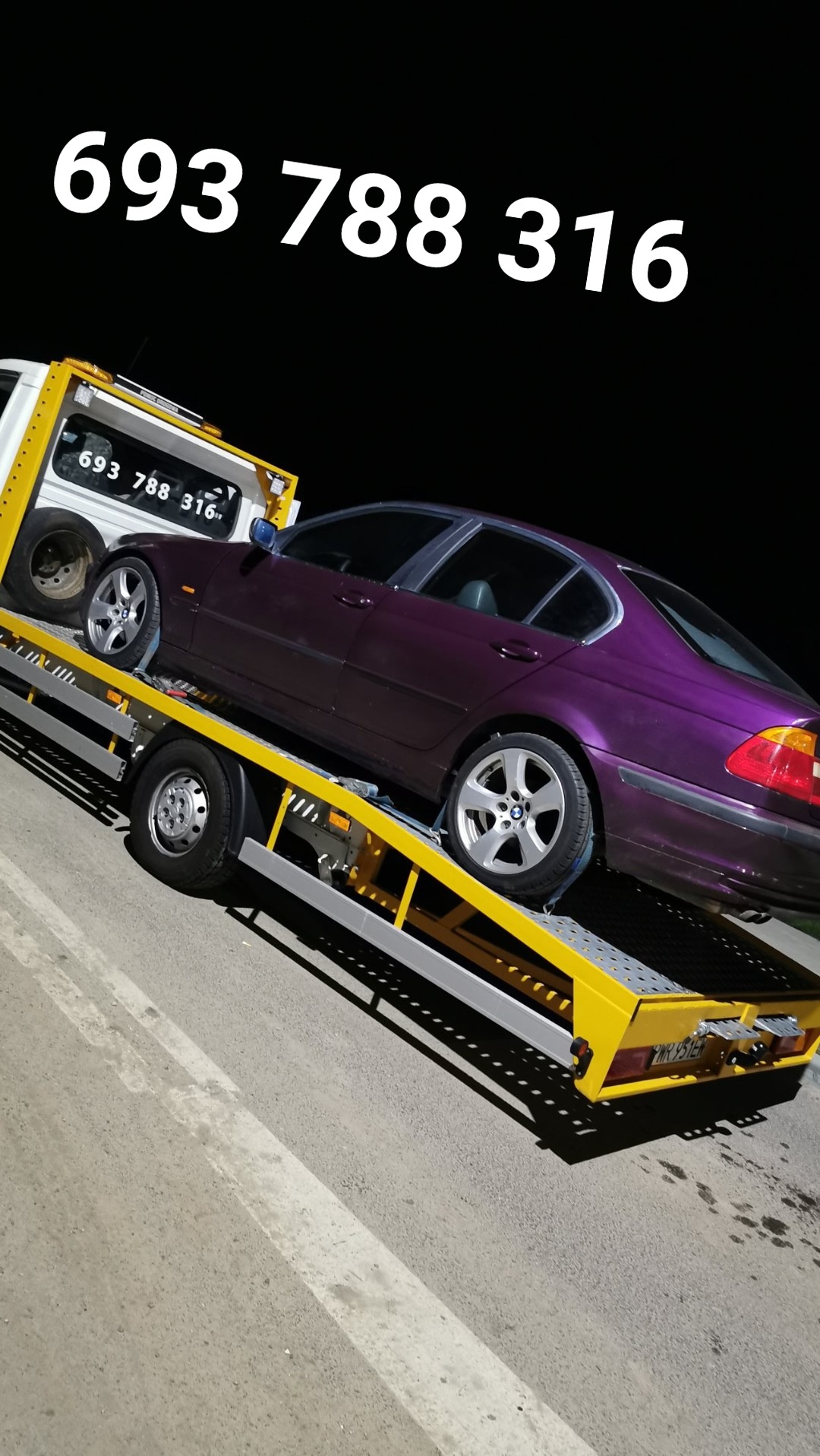 Fioletowy samochód BMW na żółtej lawecie transportowej w nocy, z numerem telefonu widocznym na lawecie i niebie.