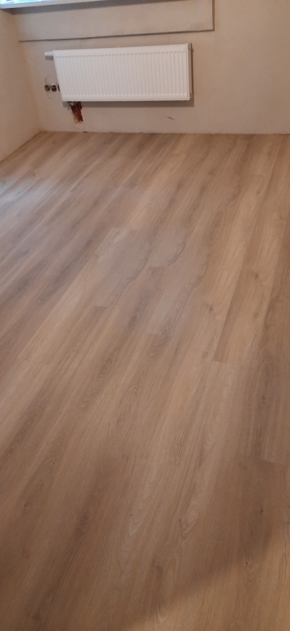 Jasne panele podłogowe ułożone w pokoju, widoczny biały grzejnik na ścianie.
