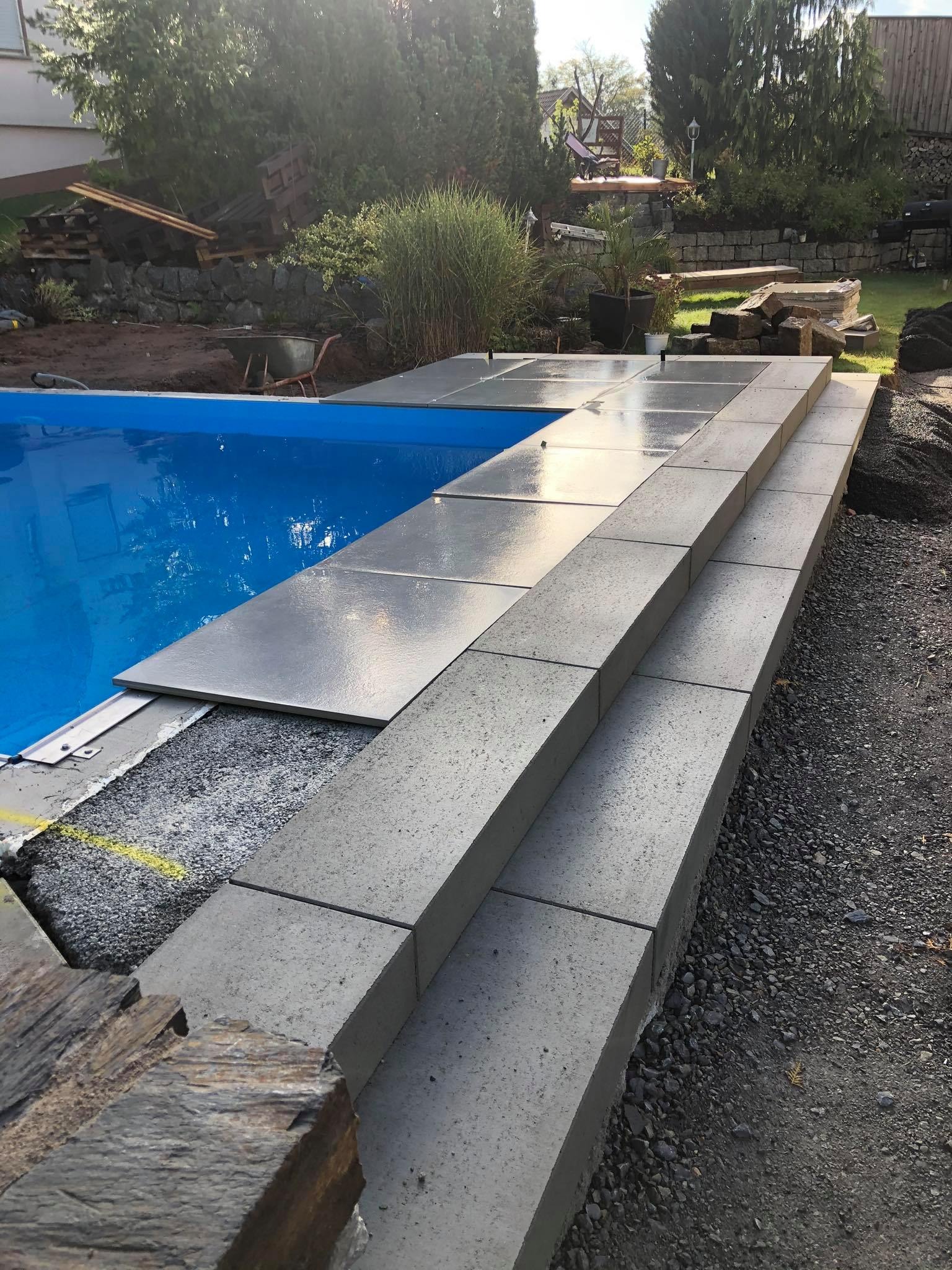 Schody z betonowych płyt prowadzące do basenu w ogrodzie, widoczne przygotowane podłoże i elementy wykończeniowe.