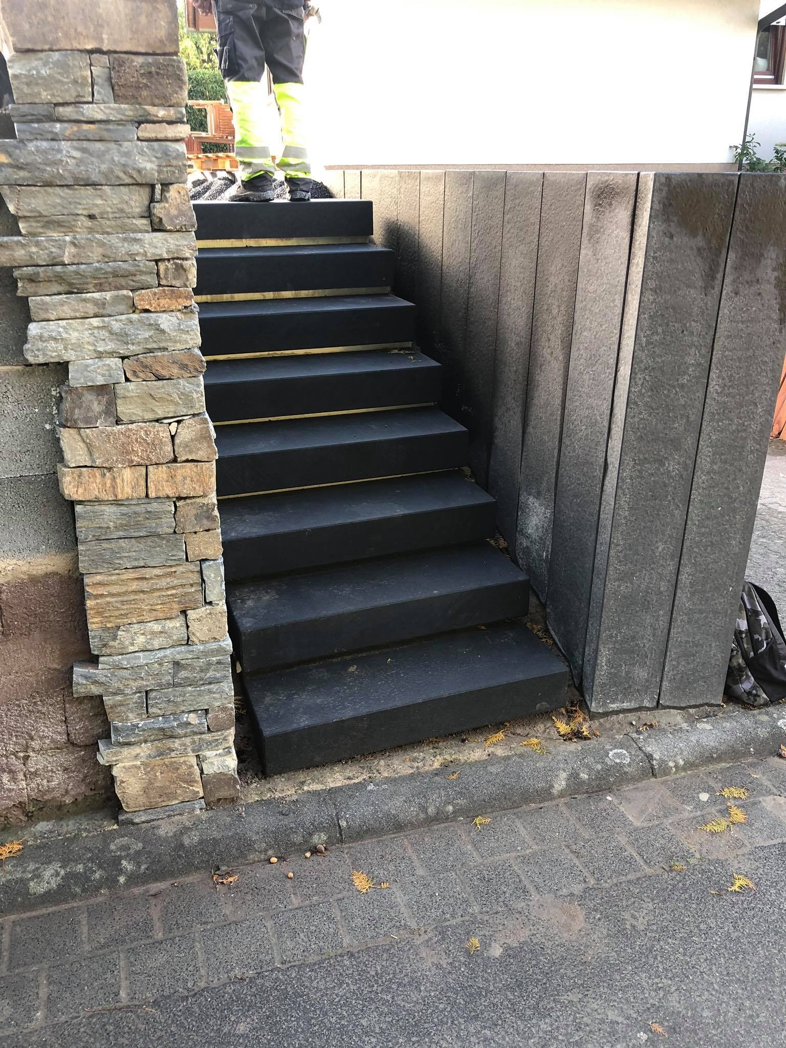 Ułożone czarne schody zewnętrzne z kamiennymi elementami wykończeniowymi, widok z poziomu chodnika.