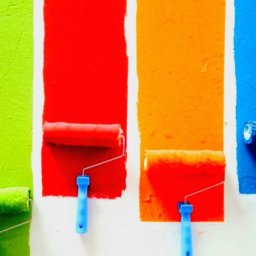 Art-dom Adam Wróblewski - Świeżo pomalowane pasy w kolorach zielonym, czerwonym, pomarańczowym i niebieskim, z wałkami do malowania w tych samych kolorach, pozostawionymi na ścianie.
