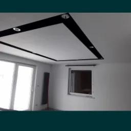 Biały sufit podwieszany z czarną ramą i wbudowanymi punktowymi lampami w nowocześnie wykończonym, jasnym wnętrzu z oknami.