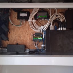 Woj-Bol Technology Wojciech Ból - Szafka z zainstalowanym sprzętem telekomunikacyjnym: router, przełączniki, zasilacze i okablowanie. Widoczne diody sygnalizacyjne na urządzeniach.