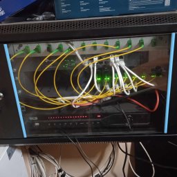 Woj-Bol Technology Wojciech Ból - Szafa rack z urządzeniami sieciowymi: switch TP-Link, rejestrator BCS. Widoczne kable światłowodowe i ethernetowe. Klucze w zamku szafy.