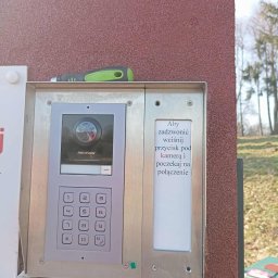 Woj-Bol Technology Wojciech Ból - Zamontowany wideodomofon Hikvision z kamerą i klawiaturą numeryczną na elewacji budynku. Nad urządzeniem leży śrubokręt. Widoczna instrukcja obsługi.