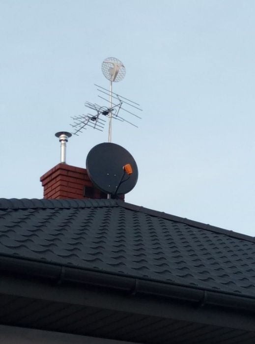 Różne typy anten (satelitarna, telewizyjna, siatkowa) zamontowane na kominie i dachu pokrytym gontem bitumicznym.