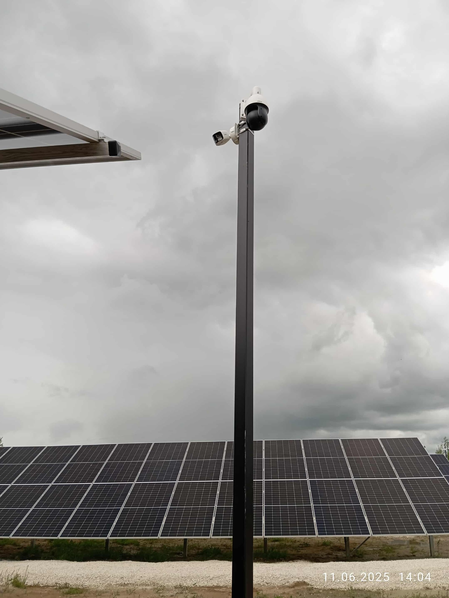 Dwie kamery monitoringu na słupie, panele słoneczne w tle, pochmurne niebo. Zestaw do monitoringu zasilany energią słoneczną.