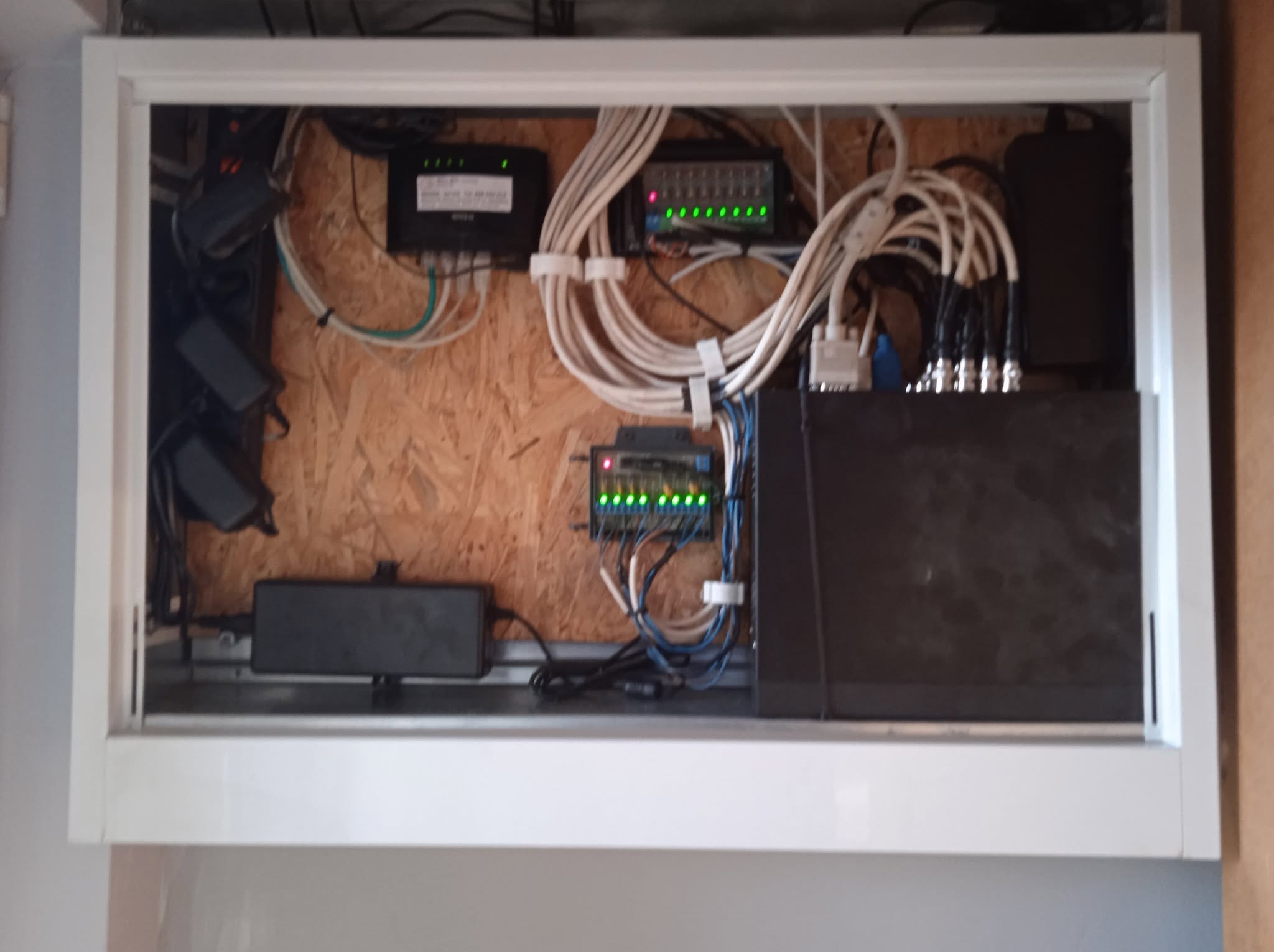 Szafka z zainstalowanym sprzętem telekomunikacyjnym: router, przełączniki, zasilacze i okablowanie. Widoczne diody sygnalizacyjne na urządzeniach.