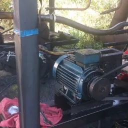 Przenośny agregat z silnikiem elektrycznym i sprężarką, zamontowany na metalowej konstrukcji, widoczne ślady smarów i brudu.