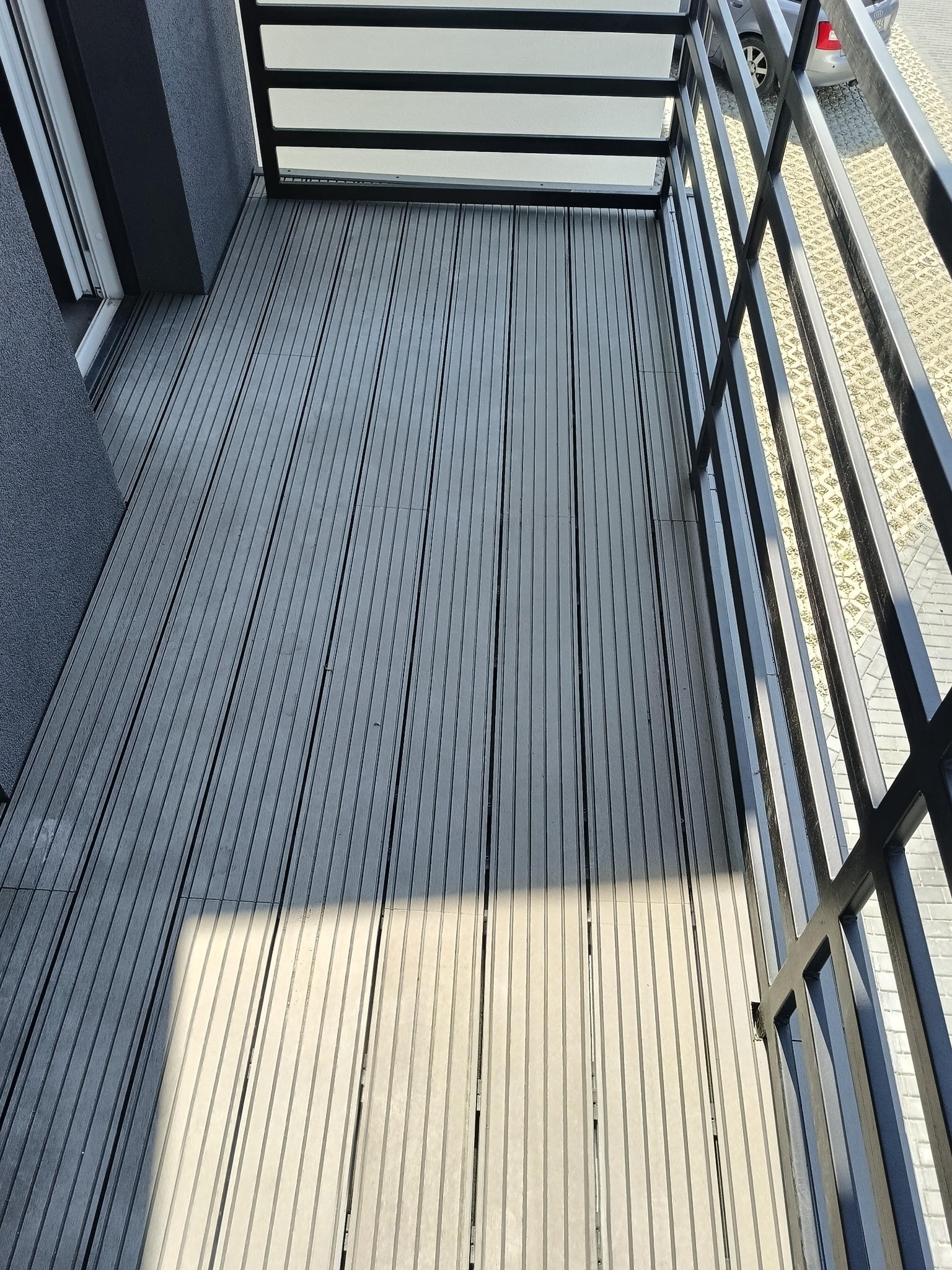 Nowoczesny balkon z szarą deską kompozytową i czarną balustradą. Widok z góry, oświetlony słońcem. Eleganckie wykończenie balkonu.