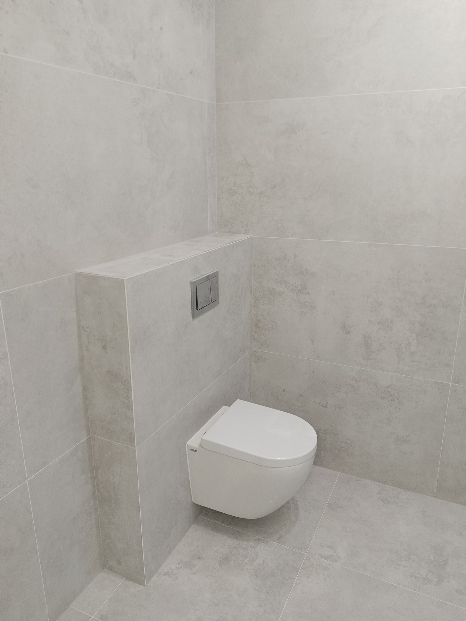 Minimalistyczna łazienka: podwieszana miska WC z szarymi płytkami imitującymi kamień, ukryty system spłukiwania. Nowoczesny design, czyste linie.