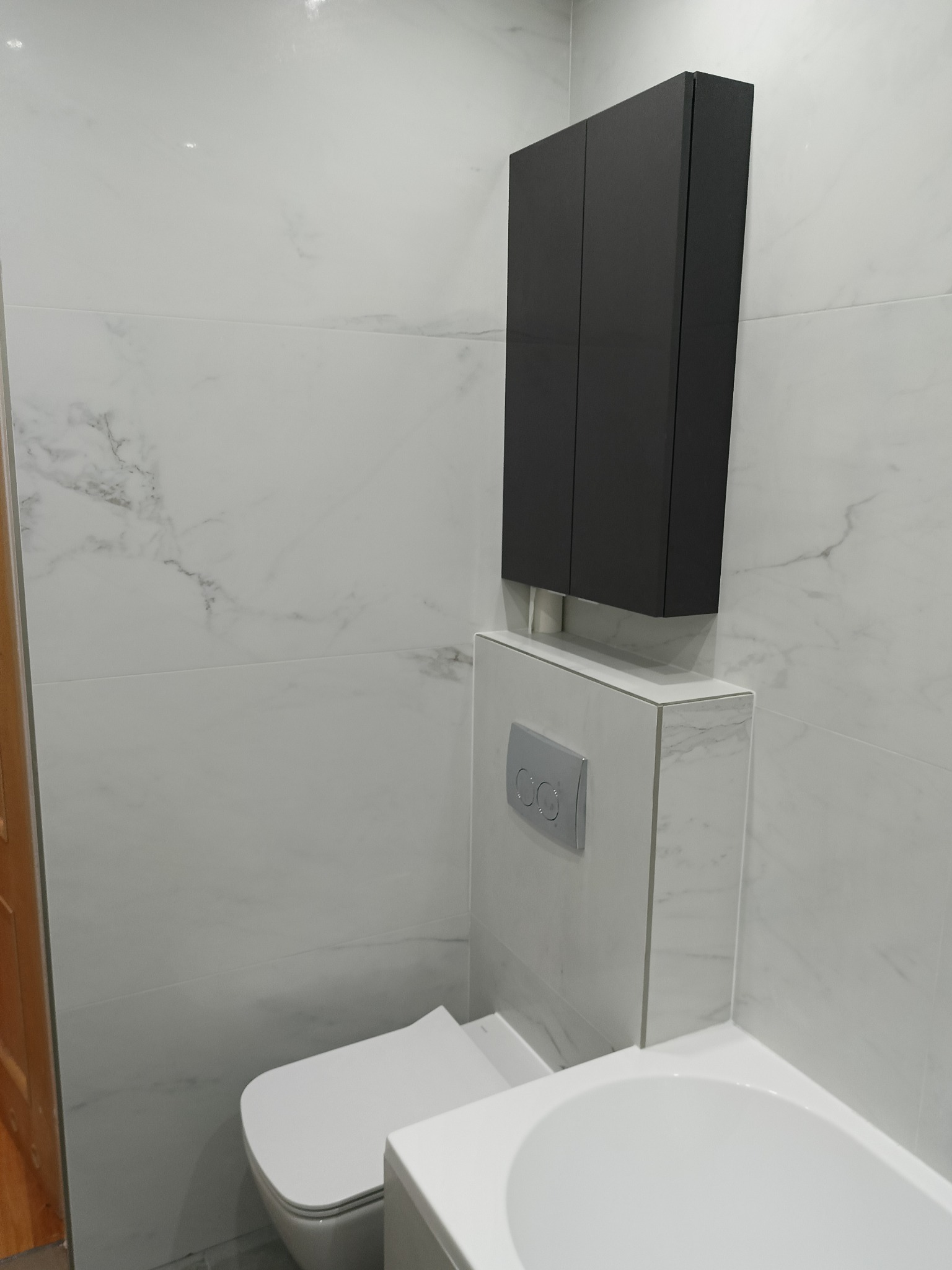 Wykończona łazienka w Mielcu: białe płytki imitujące marmur, podwieszana toaleta z szarym szafką. Nowoczesny design i funkcjonalność w jednym.