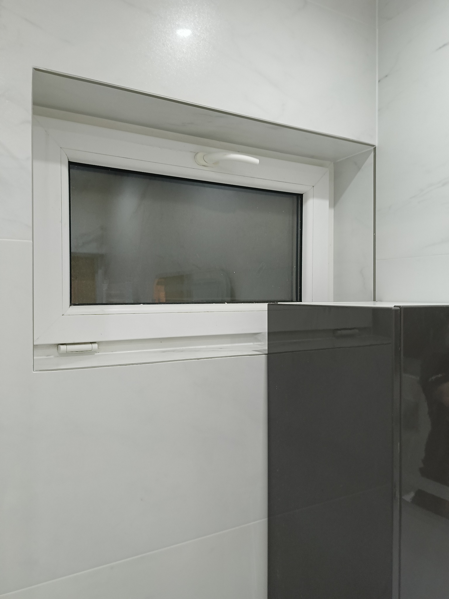 Białe okno PCV w łazience z marmurowymi płytkami i szarą szafką. Widok na fragment wnętrza po remoncie, z dbałością o detale wykończeniowe.