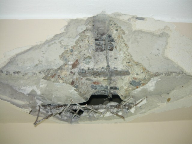 Uszkodzony strop betonowy z odsłoniętym zbrojeniem w mieszkaniu w Warszawie, widoczne kruszywo i ubytki betonu.