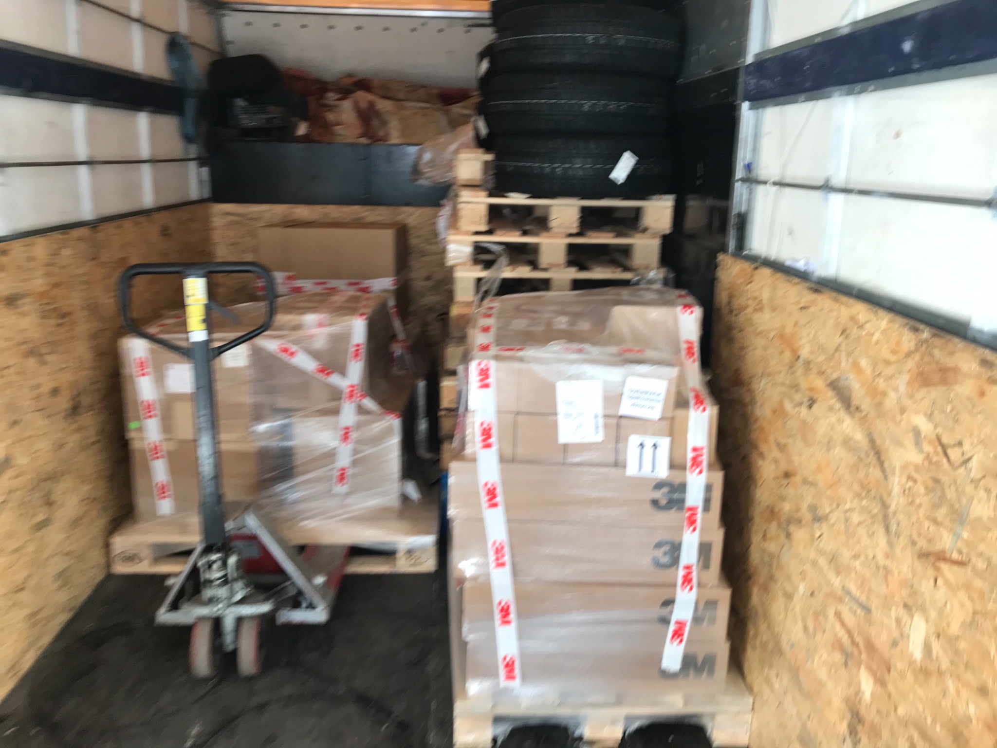 Wnętrze busa we Wrocławiu, załadowane paletami z kartonami zabezpieczonymi folią i taśmą, obok wózek paletowy, w tle opony ułożone na palecie.