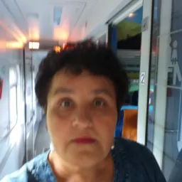 Portret kobiety w dżinsowej kurtce na tle wnętrza wagonu pociągu z widoczną toaletą i przedziałami.