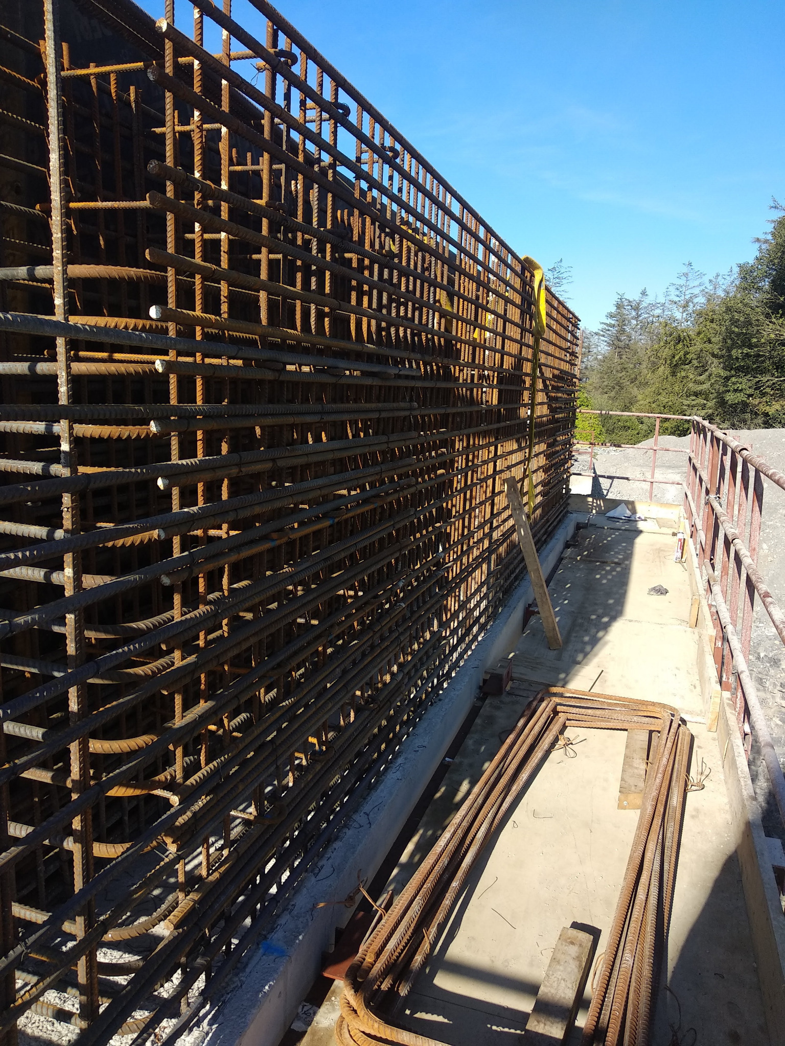 Siatka zbrojeniowa ułożona w szalunku, widoczne pręty zbrojeniowe, betonowy fundament i fragment krajobrazu w tle.