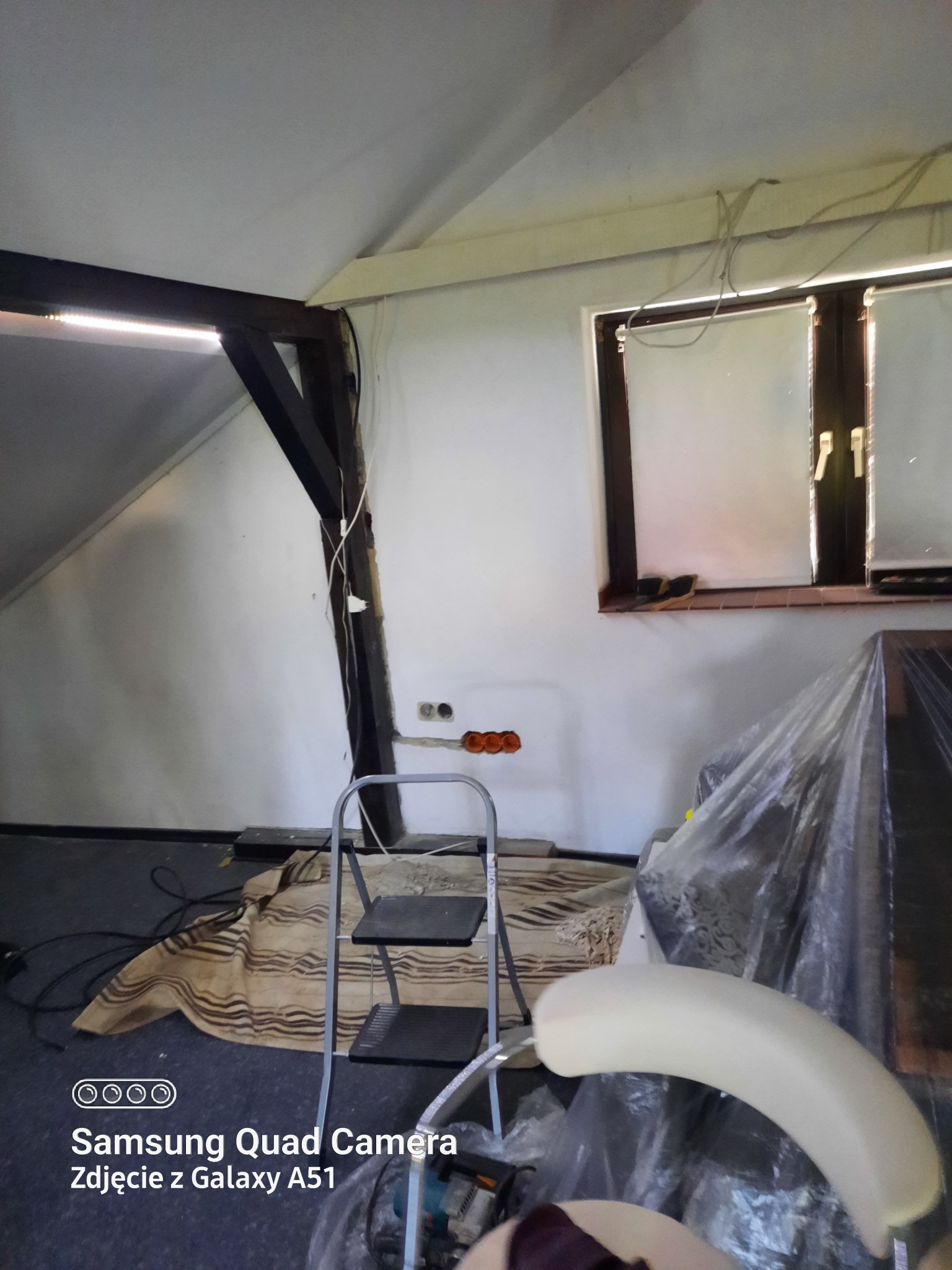 Poddasze w trakcie prac: widoczne przewody elektryczne, puszki instalacyjne, drabina i zabezpieczone folią meble.