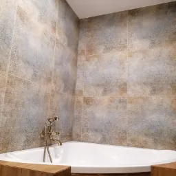 Biała narożna wanna obudowana drewnem, z baterią w stylu retro na tle ściany wyłożonej dekoracyjnymi płytkami w odcieniach beżu i szarości.