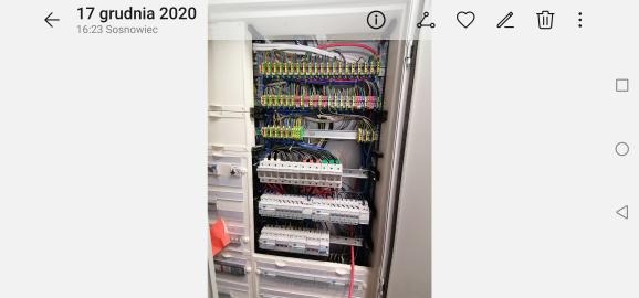 Rozdzielnica elektryczna w szafce, widoczne liczne przewody, bezpieczniki i złączki, schludnie ułożone.