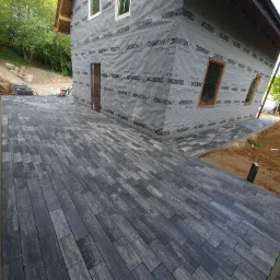 Ułożona, szara kostka brukowa prowadząca do domu w trakcie ocieplania, widoczna folia izolacyjna z nadrukiem CREATON.