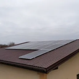 Panele fotowoltaiczne zamontowane na brązowym dachu z blachy falistej domu jednorodzinnego w pochmurny dzień.