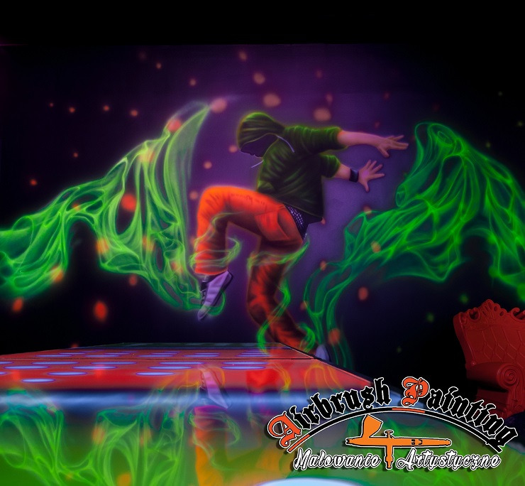 Fluorescencyjna scena z tancerzem w ruchu, otoczonym zielonymi, abstrakcyjnymi kształtami, wykonana techniką airbrush na czarnym tle z efektem gwiazd, podświetlona światłem UV.