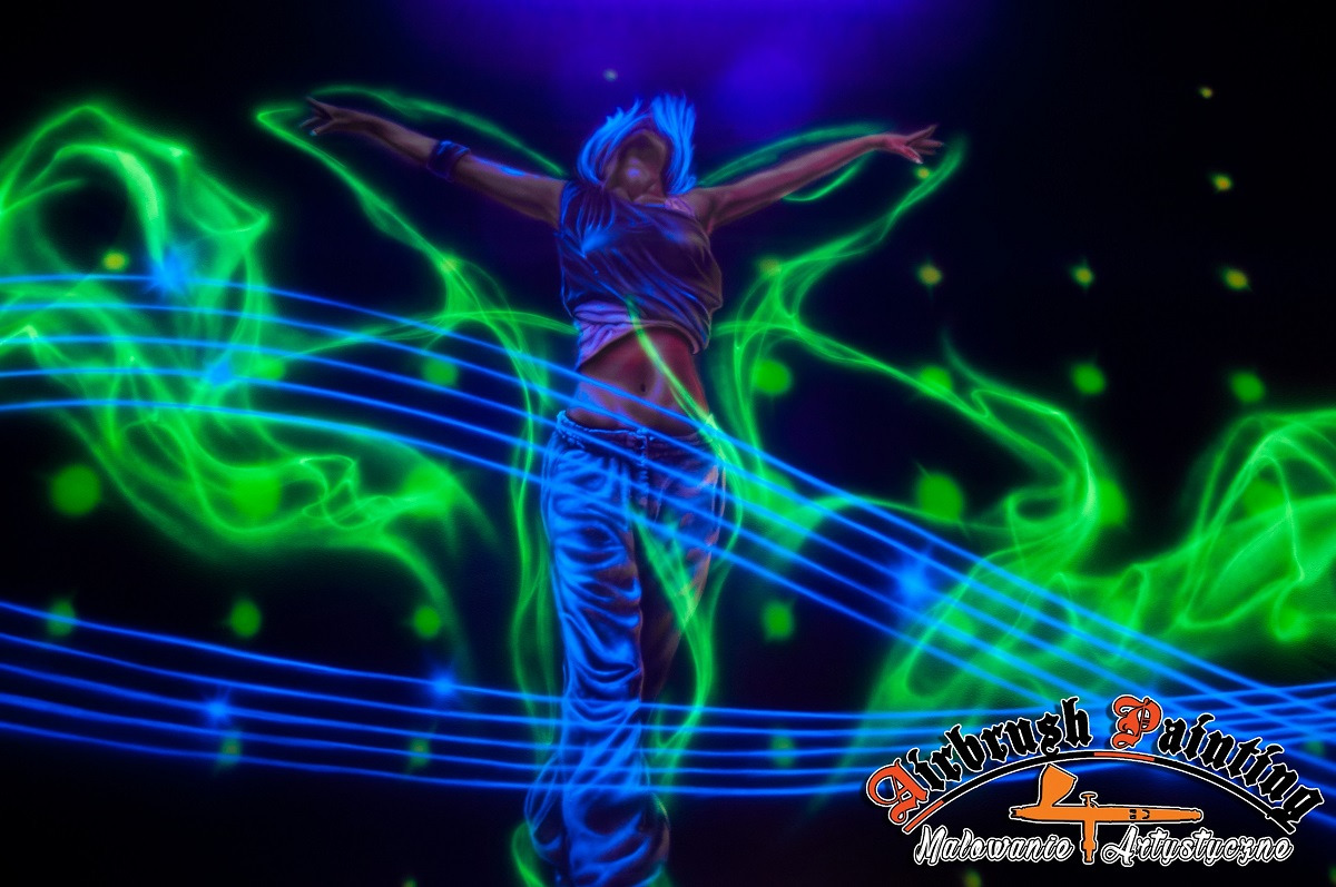 Iluminacja UV przedstawiająca postać kobiety z rozłożonymi ramionami, otoczoną zielonymi i niebieskimi świetlnymi efektami na czarnym tle, z widocznym logo firmy specjalizującej się w malowaniu...