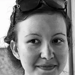 Portret uśmiechniętej kobiety w okularach przeciwsłonecznych na głowie, czarno-białe zdjęcie z bliska.