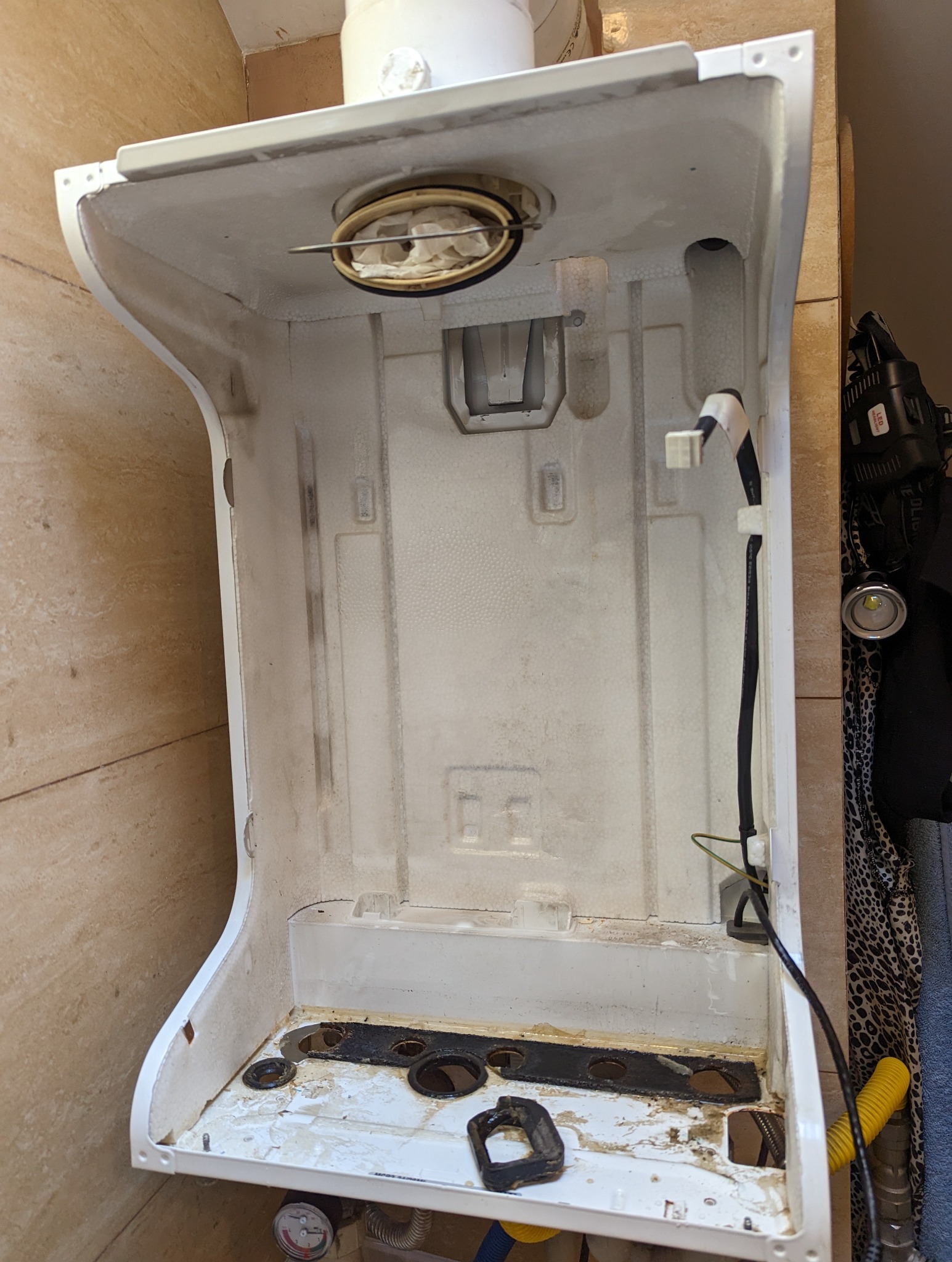 Wnętrze obudowy pieca gazowego z widocznymi śladami użytkowania i osadami, zdemontowane elementy palnika w górnej części, przewody elektryczne po prawej stronie i przyłącza gazowe na dole.