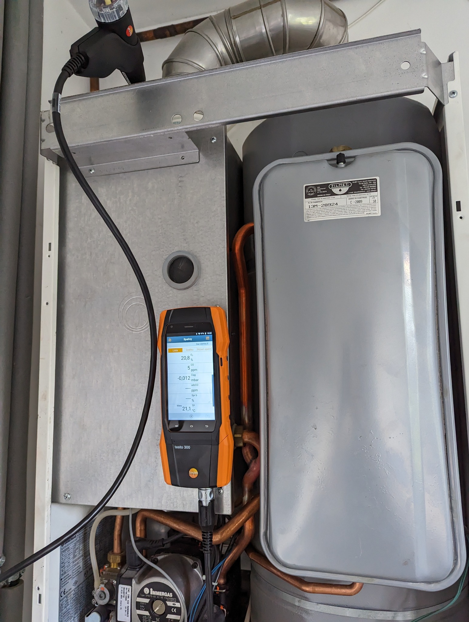 Analizator spalin Testo 300 podłączony do pieca gazowego Immergas, wyświetlający wartości pomiarowe na ekranie, widoczne rury miedziane i elementy kotła.