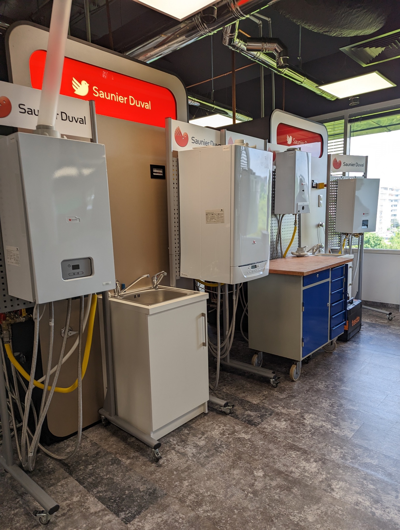 Ekspozycja kilku modeli pieców gazowych marki Saunier Duval w showroomie, z widocznymi przyłączami i narzędziami serwisowymi.