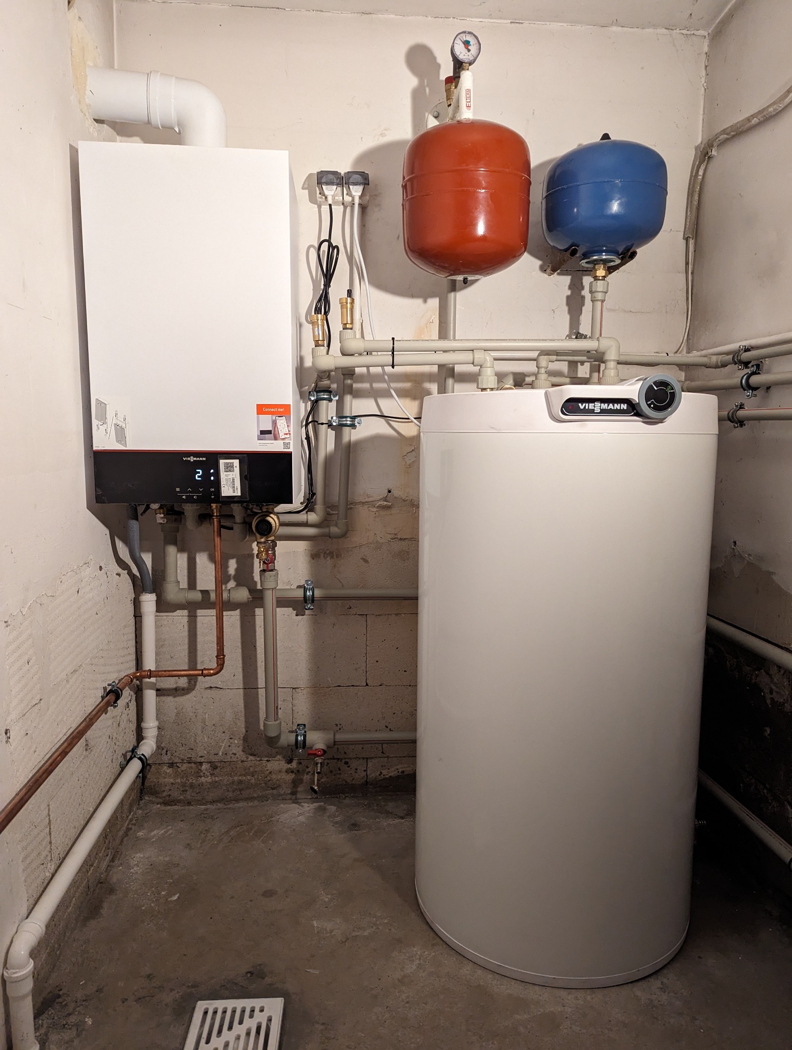 Nowoczesny, kondensacyjny piec gazowy Viessmann zamontowany w kotłowni, z widocznymi elementami instalacji, w tym zbiornikami wyrównawczymi w kolorach czerwonym i niebieskim oraz rurami miedzianymi.