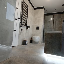 Pro-Gres Artur Kowalski - Nowoczesna łazienka wykończona w szarościach, z podwieszaną toaletą, grzejnikiem drabinkowym w kolorze czarnym i kabiną prysznicową z czarnymi ramami. Na podłodze płytki z delikatnym wzorem.