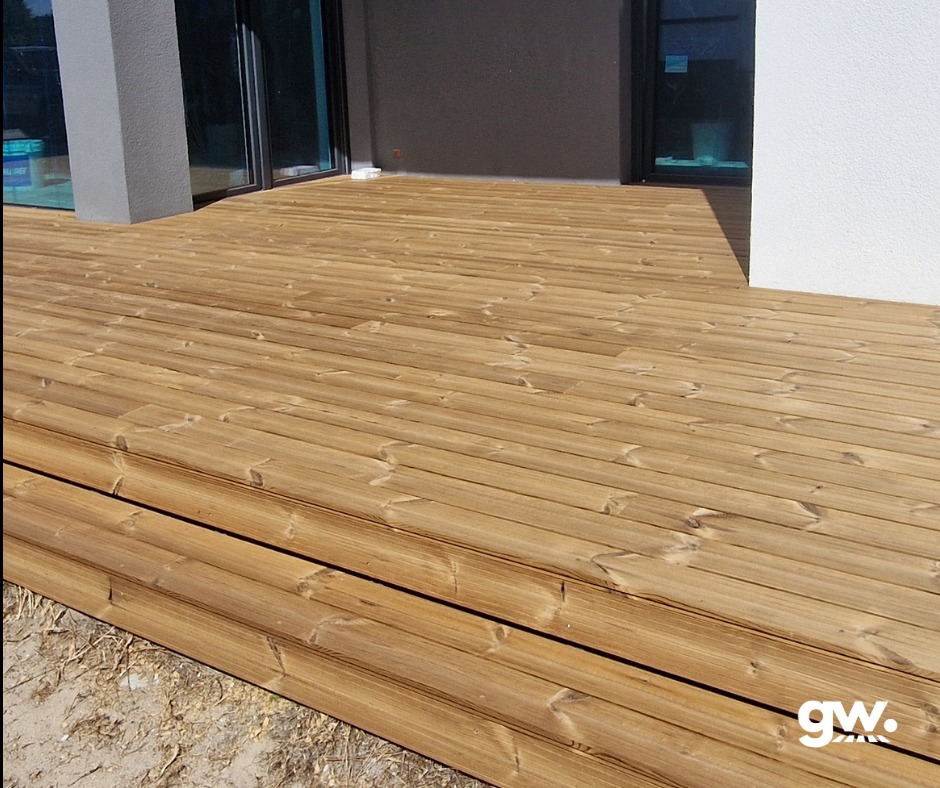 Gotowy taras z desek thermososna, widok z poziomu gruntu, z fragmentami elewacji budynku w tle.