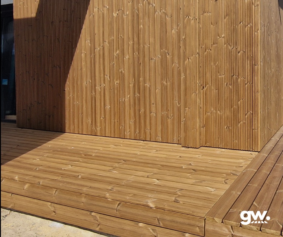 Wykończony taras z desek thermososna, z widoczną elewacją budynku wykonaną z tego samego materiału, oświetlony naturalnym światłem słonecznym.