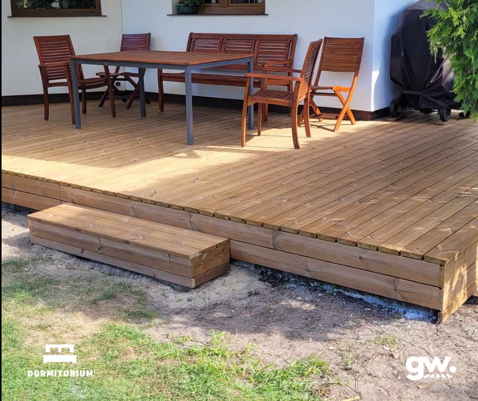 Gotowy taras z deski thermososna w Nakle nad Notecią, z niskimi schodkami prowadzącymi na trawnik, wyposażony w drewniane meble ogrodowe.